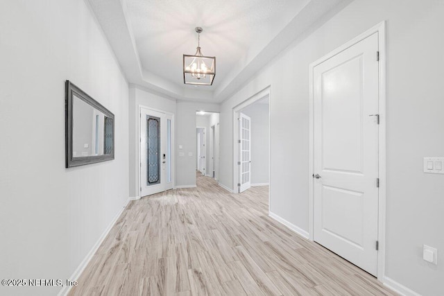 foyer entrance featuring a tray ceiling, a chandelier, and light wood-type flooring