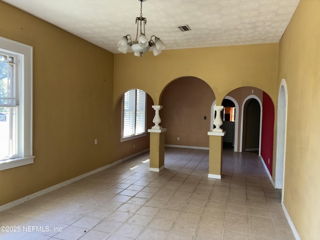 tiled empty room with a textured ceiling and a chandelier