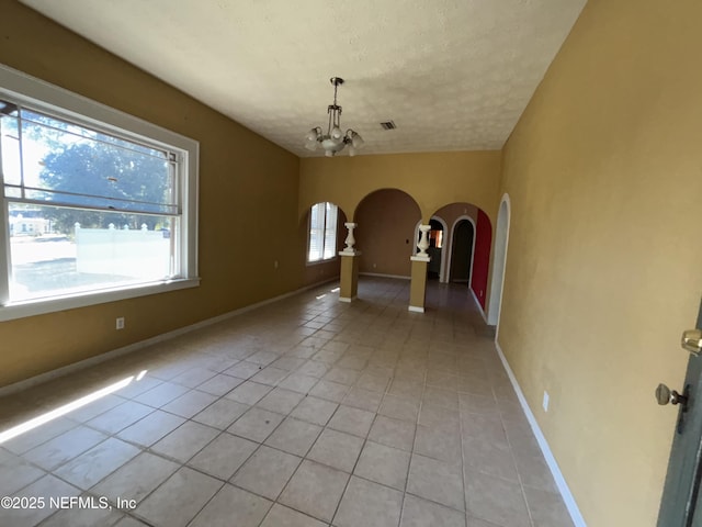 unfurnished dining area with an inviting chandelier, a textured ceiling, and light tile patterned flooring