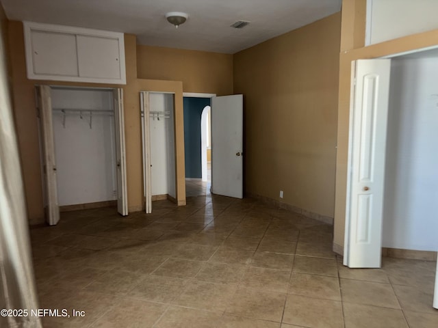 unfurnished bedroom featuring light tile patterned floors and two closets