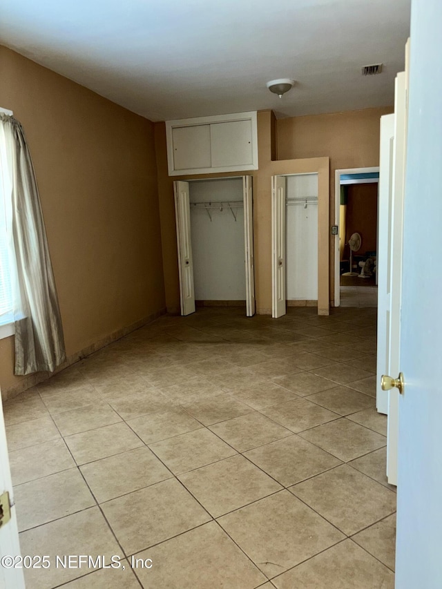 unfurnished bedroom featuring light tile patterned floors and multiple closets