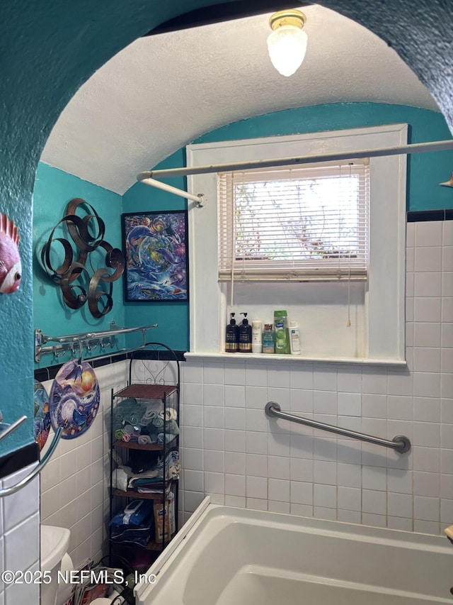 bathroom with vaulted ceiling, tile walls, a textured ceiling, and toilet