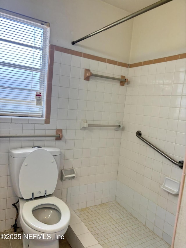 bathroom with a tile shower, tile walls, and toilet