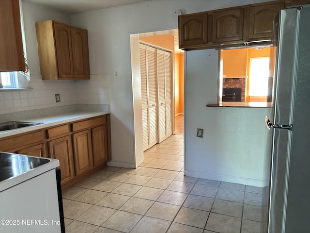 kitchen with light tile patterned flooring, stainless steel refrigerator, sink, decorative backsplash, and white range oven