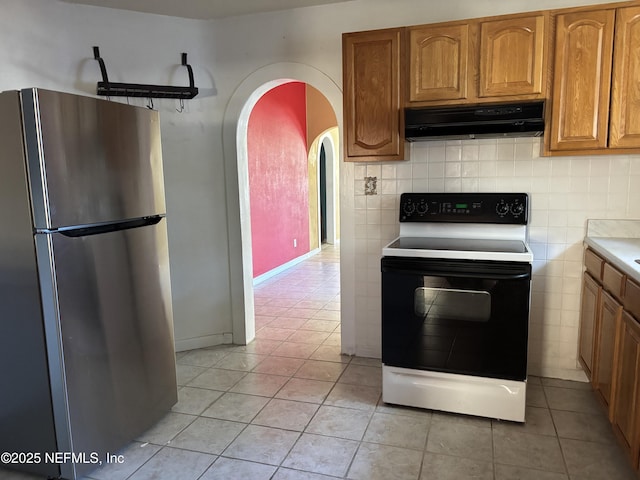 kitchen featuring light tile patterned floors, electric range, stainless steel refrigerator, and decorative backsplash