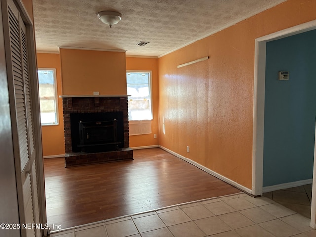 unfurnished living room featuring crown molding, a fireplace, a textured ceiling, and light wood-type flooring