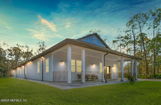 rear view of house featuring a porch, a lawn, and board and batten siding