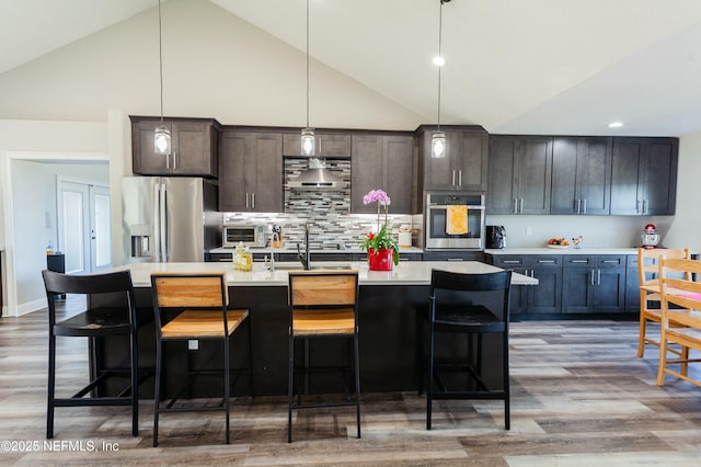 kitchen featuring dark brown cabinets, stainless steel appliances, wall chimney exhaust hood, and a center island with sink