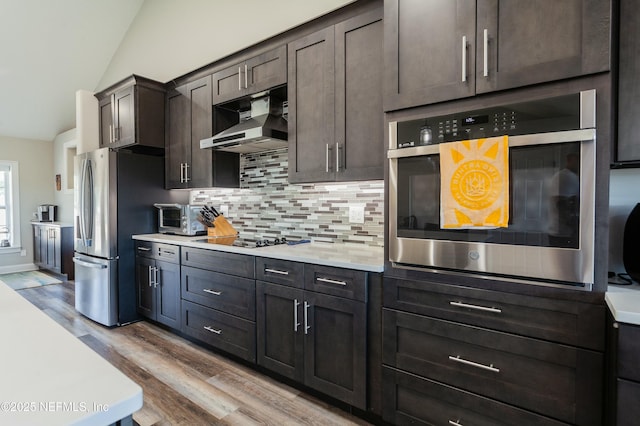 kitchen featuring vaulted ceiling, dark brown cabinets, light hardwood / wood-style flooring, appliances with stainless steel finishes, and decorative backsplash