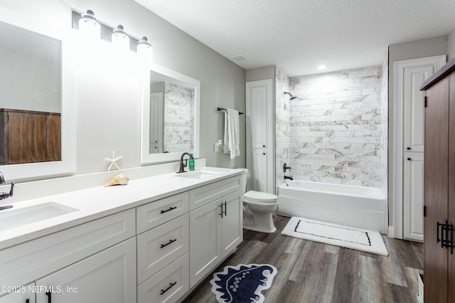 full bathroom featuring hardwood / wood-style floors, tiled shower / bath combo, vanity, toilet, and a textured ceiling