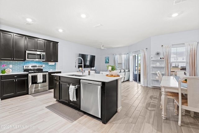 kitchen featuring sink, light wood-type flooring, appliances with stainless steel finishes, ceiling fan, and a kitchen island with sink