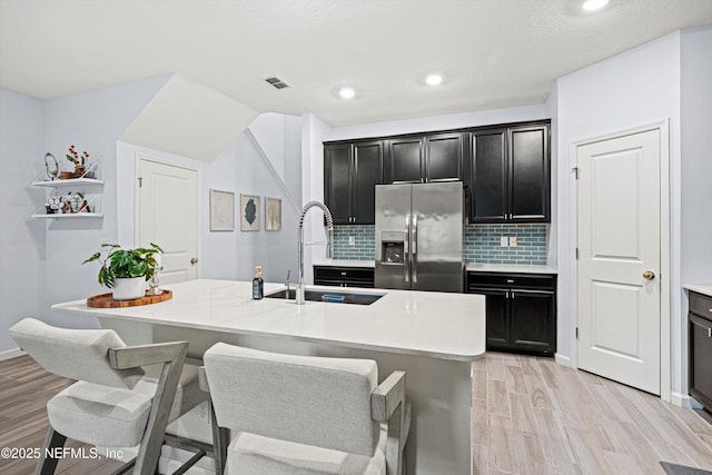 kitchen featuring a breakfast bar, sink, backsplash, stainless steel fridge with ice dispenser, and a center island with sink