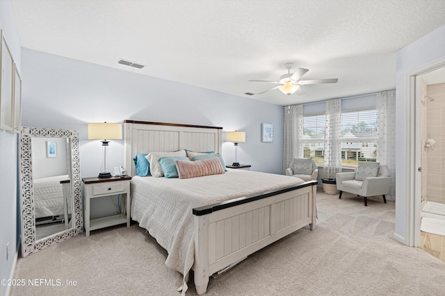 bedroom with ceiling fan, light colored carpet, a textured ceiling, and ensuite bath