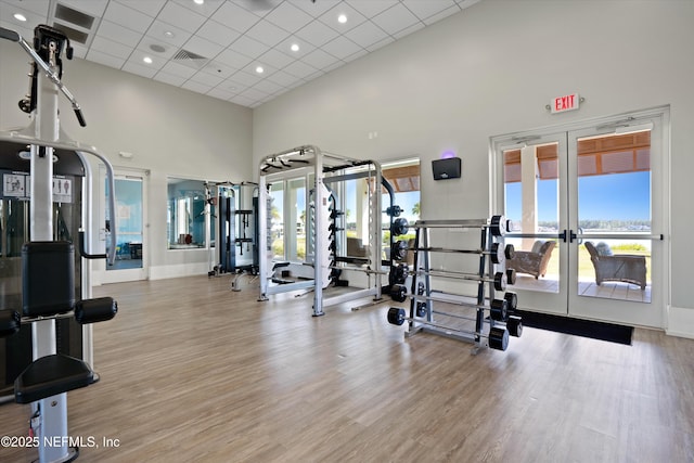 gym featuring french doors, a towering ceiling, light hardwood / wood-style floors, and a drop ceiling