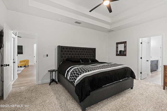 bedroom with a tray ceiling, visible vents, a ceiling fan, light carpet, and baseboards