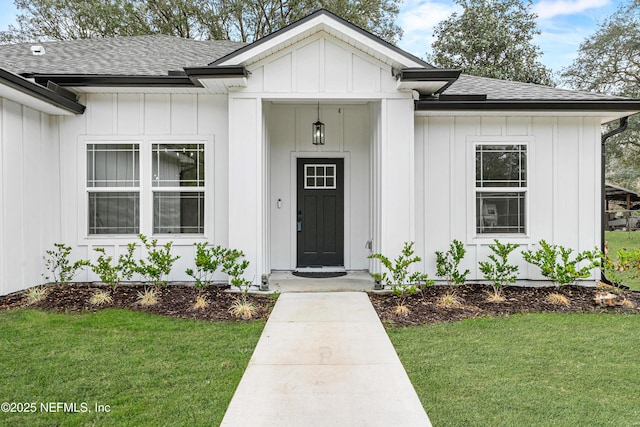 view of exterior entry featuring roof with shingles, a yard, and board and batten siding