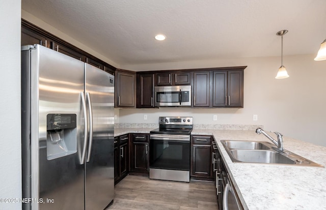 kitchen with sink, appliances with stainless steel finishes, hanging light fixtures, dark brown cabinets, and wood-type flooring