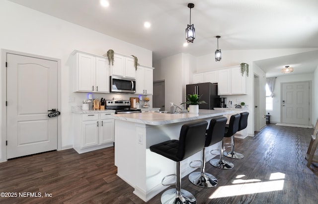 kitchen featuring lofted ceiling, white cabinets, hanging light fixtures, stainless steel appliances, and a center island with sink