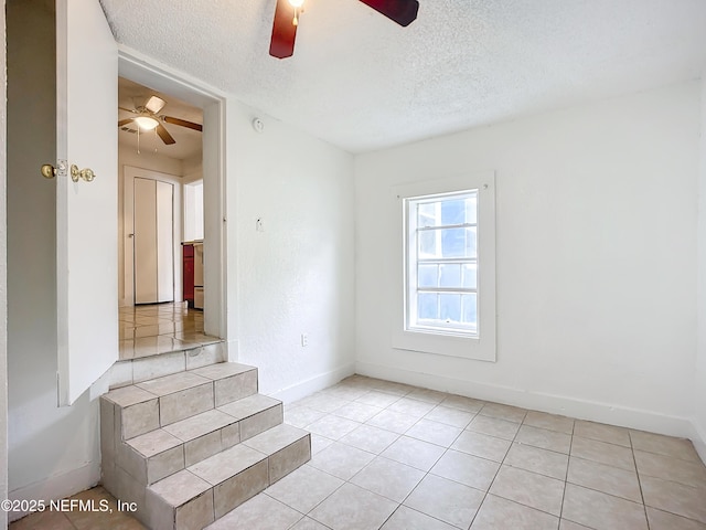 tiled empty room with ceiling fan and a textured ceiling