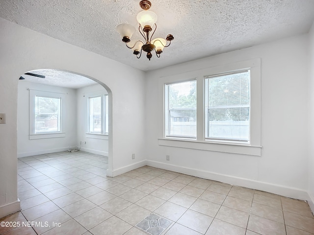 tiled empty room with a textured ceiling and a notable chandelier