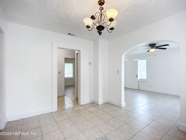 tiled empty room with ceiling fan with notable chandelier, a textured ceiling, and a healthy amount of sunlight