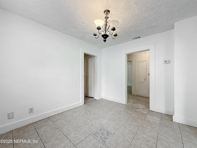 empty room with light tile patterned flooring, a textured ceiling, and an inviting chandelier