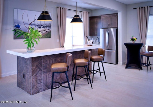 kitchen with stainless steel refrigerator, decorative light fixtures, a breakfast bar area, kitchen peninsula, and dark brown cabinets