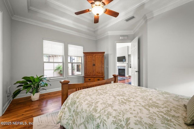 bedroom with crown molding, dark wood-type flooring, ceiling fan, and a tray ceiling