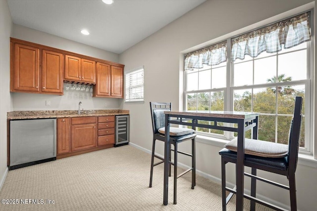 kitchen with sink, stainless steel fridge, beverage cooler, light colored carpet, and light stone countertops