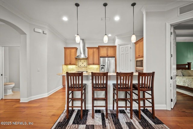 kitchen with stainless steel fridge, a kitchen breakfast bar, black microwave, and wall chimney exhaust hood