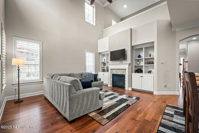 living room featuring built in features, ornamental molding, dark hardwood / wood-style floors, and a stone fireplace