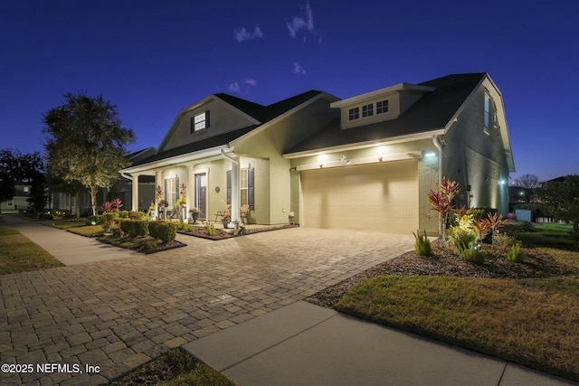 view of front of property with decorative driveway, an attached garage, and stucco siding