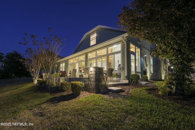 property exterior at twilight with a sunroom and a lawn