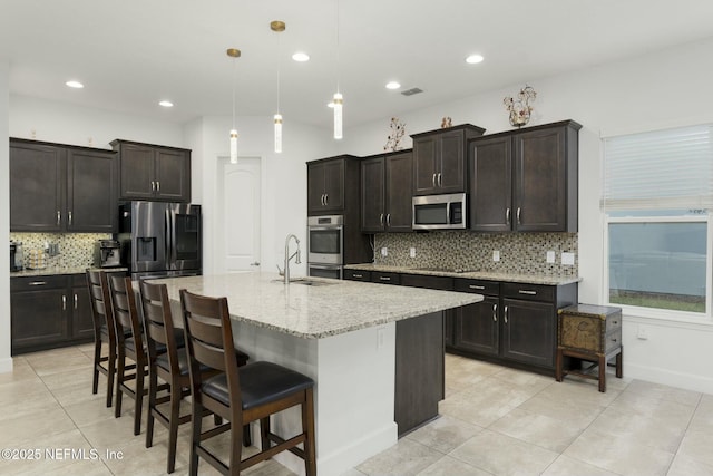 kitchen featuring a kitchen island with sink, hanging light fixtures, backsplash, and stainless steel appliances