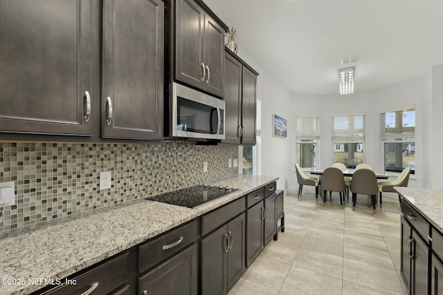 kitchen with light tile patterned floors, dark brown cabinetry, black electric stovetop, light stone countertops, and decorative backsplash