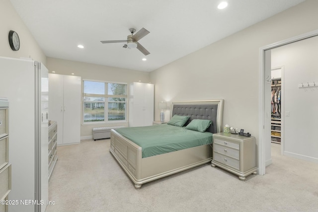 bedroom with ceiling fan, white refrigerator, a spacious closet, light colored carpet, and a closet