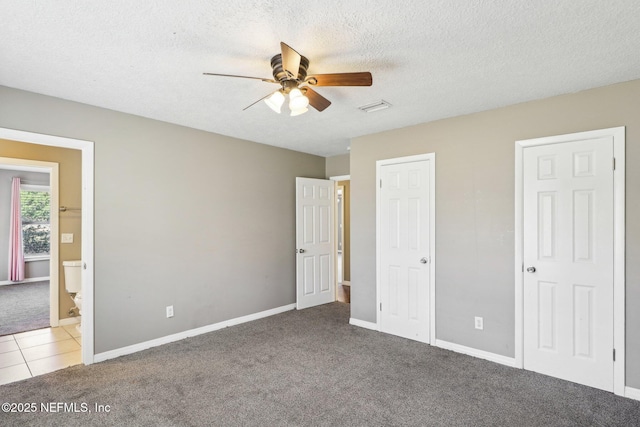 unfurnished bedroom featuring ensuite bath, carpet floors, ceiling fan, multiple closets, and a textured ceiling