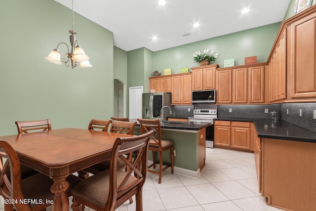 kitchen with a breakfast bar area, a kitchen island with sink, backsplash, stainless steel appliances, and decorative light fixtures