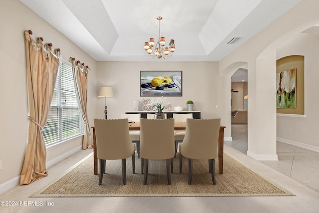 tiled dining room with a tray ceiling and a chandelier