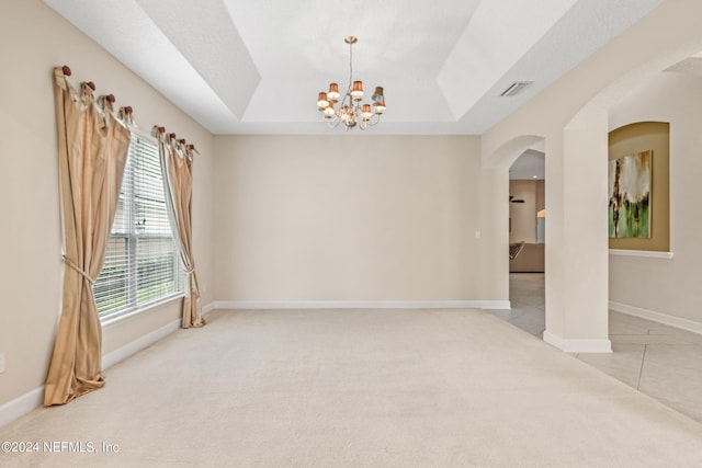 empty room featuring light colored carpet, a raised ceiling, and a chandelier