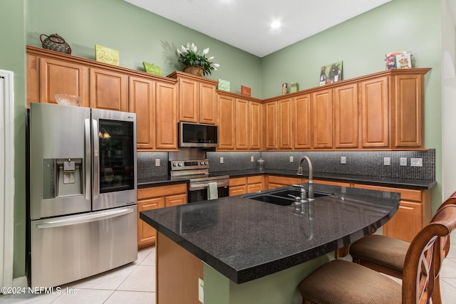 kitchen with sink, a breakfast bar area, light tile patterned floors, stainless steel appliances, and a kitchen island with sink