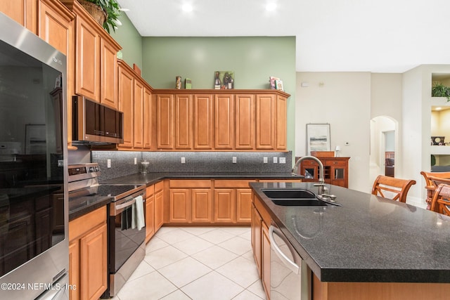 kitchen with an island with sink, appliances with stainless steel finishes, sink, and backsplash