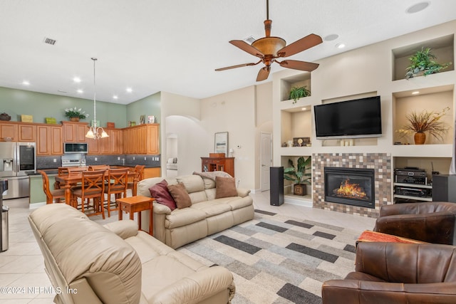 living room with a tiled fireplace, light tile patterned floors, ceiling fan, and a high ceiling