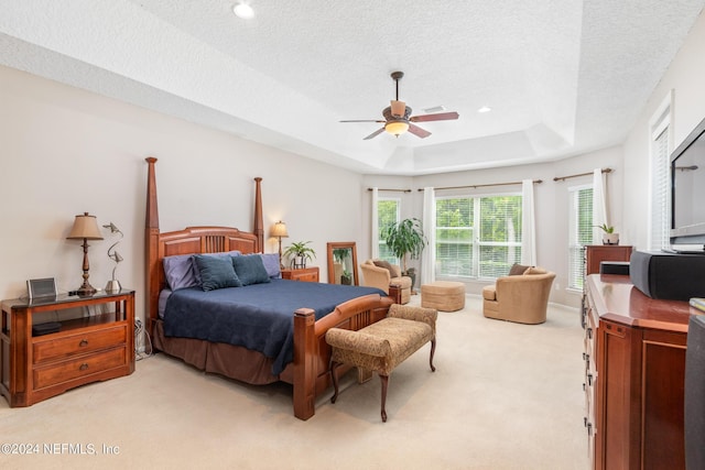 bedroom with ceiling fan, light colored carpet, a tray ceiling, and a textured ceiling