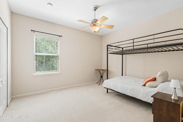 bedroom with ceiling fan, light colored carpet, and a textured ceiling