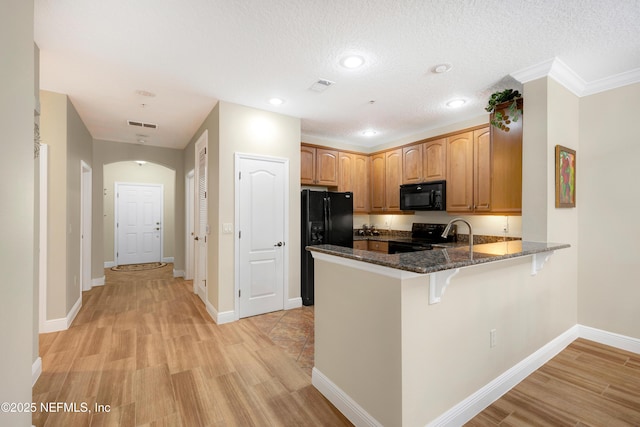 kitchen featuring kitchen peninsula, a textured ceiling, dark stone counters, and black appliances