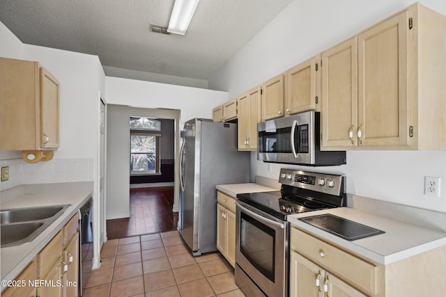 kitchen with sink, a textured ceiling, light brown cabinets, light tile patterned floors, and appliances with stainless steel finishes