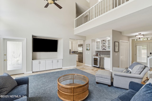 living room featuring a towering ceiling, beverage cooler, ceiling fan, and bar area