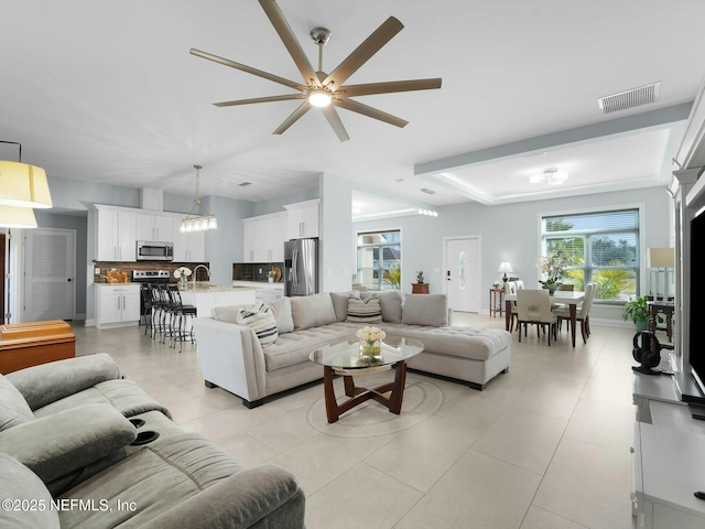 tiled living room with ceiling fan, a raised ceiling, and sink