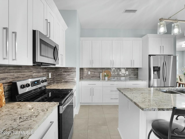 kitchen with pendant lighting, appliances with stainless steel finishes, white cabinetry, a kitchen breakfast bar, and decorative backsplash